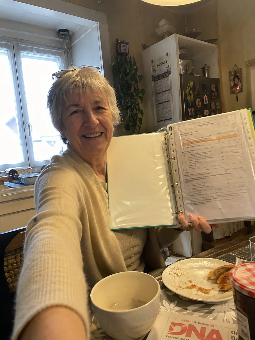 Une cliente du Protocole 48-15-6 souriante, montrant son classeur familial rempli, dans sa cuisine